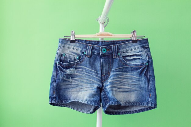 Nahaufnahme von Jeans-Shorts in einem Kleiderbügel isoliert auf grünem Hintergrund