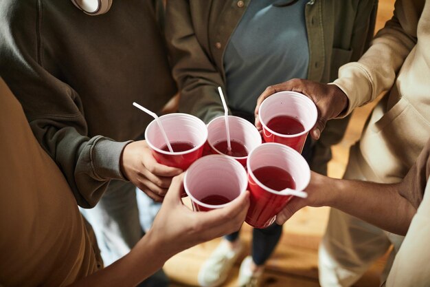 Nahaufnahme von jungen Leuten, die auf einer Party mit Plastikbechern mit alkoholischen Getränken anstoßen