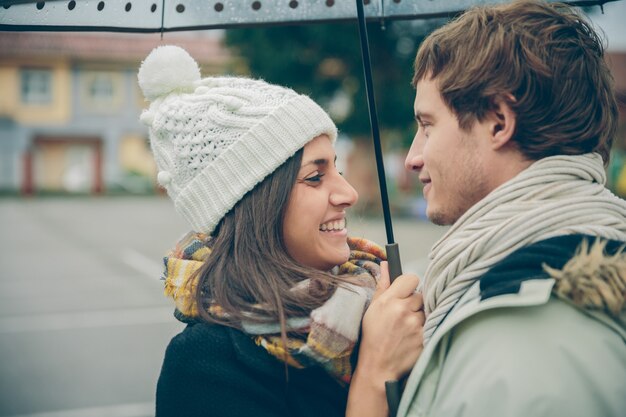 Nahaufnahme von jungen schönen Paaren, die an einem regnerischen Herbsttag unter dem Regenschirm umarmen und lachen. Liebes- und Paarbeziehungskonzept.