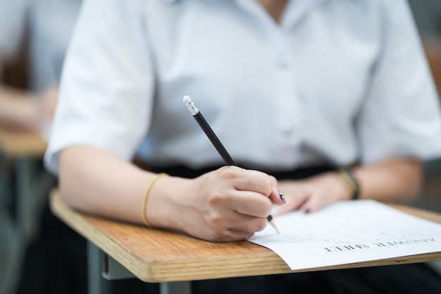 Nahaufnahme von jungen Studenten konzentrieren sich auf die Prüfung im Klassenzimmer. Studentin schreibt auf dem Prüfungsantwortpapier im Klassenzimmer.