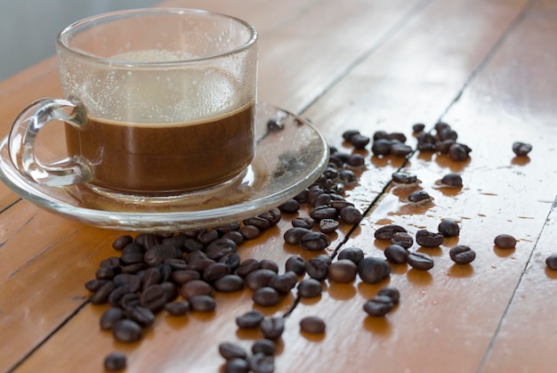 Nahaufnahme von Kaffeebohnen und einer Tasse auf einem Holztisch