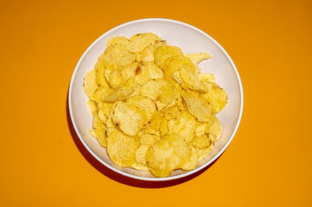 Nahaufnahme von Kartoffelchips oder Chips in einer Schüssel vor gelbem Hintergrund