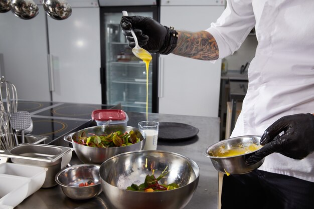 Nahaufnahme von Kochhänden, die in einer Restaurantküche Salat gießende Sauce zubereiten