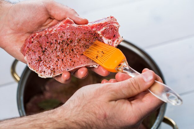 Nahaufnahme von Köchen, die das Fleisch würzen. Auflauf mit rohem Fleisch auf weißem Hintergrund.