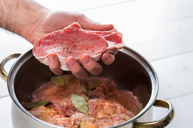 Nahaufnahme von Köchen, die das Fleisch würzen. Auflauf mit rohem Fleisch auf weißem Hintergrund.