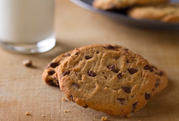 Nahaufnahme von köstlichen Keksen mit Schokoladenstückchen auf der Holzoberfläche in der Nähe eines Glases Milch