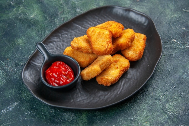 Nahaufnahme von leckeren Chicken Nuggets und Ketchup in schwarzer Platte auf dunkler Oberfläche mit freiem Platz