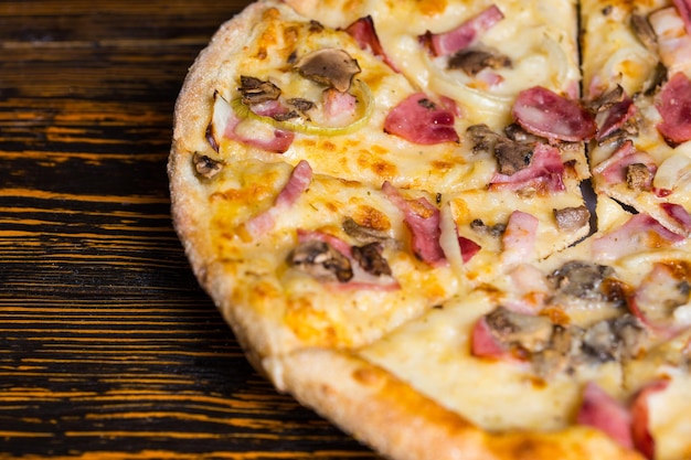 Nahaufnahme von leckerer Pizza mit Schinken, Champignons und Zwiebeln auf Holztisch