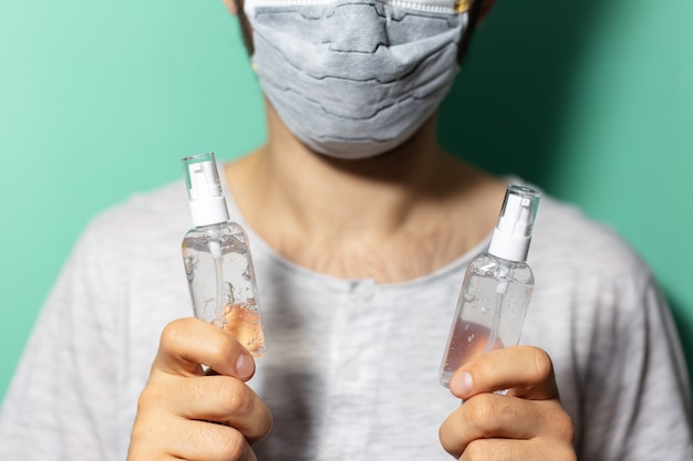 Nahaufnahme von männlichen Händen, die zwei Flaschen mit Desinfektionsgel halten, Antiseptikum für Hygiene gegen Coronavirus. Tragen einer medizinischen Gesichtsmaske auf der Oberfläche von Cyan