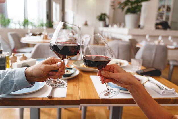 Nahaufnahme von männlichen und weiblichen Händen, die Gläser alkoholisches Getränk mit hölzernem Cafétisch anstoßen?