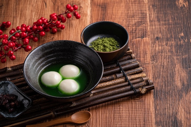 Nahaufnahme von Matcha Big Tangyuan (Tang Yuan) mit süßer Matcha-Suppe in einer Schüssel auf Holztischhintergrund für Festivalessen.