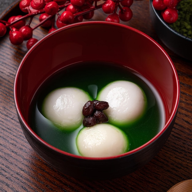 Nahaufnahme von Matcha Big Tangyuan (Tang Yuan) mit süßer Matcha-Suppe in einer Schüssel auf Holztischhintergrund für Festivalessen.