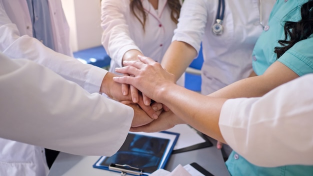 Nahaufnahme von Medizinern Stapel Hände auf dem Tisch zusammen für Unterstützung bei der Arbeit. Ärzteteam im Modern Hospital. Teamgeist bei modern in der Klinik.