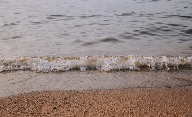 Nahaufnahme von Meereswelle mit Sonnenuntergang oder Sonnenaufgang Strand und Sand Hintergrund