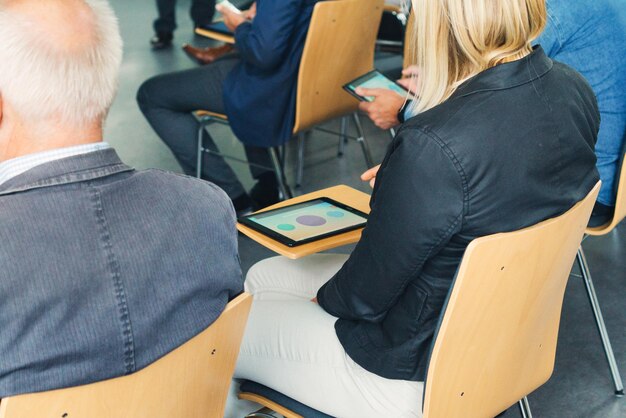 Nahaufnahme von Menschen mit digitalem Tablet, die in einem Seminar sitzen.