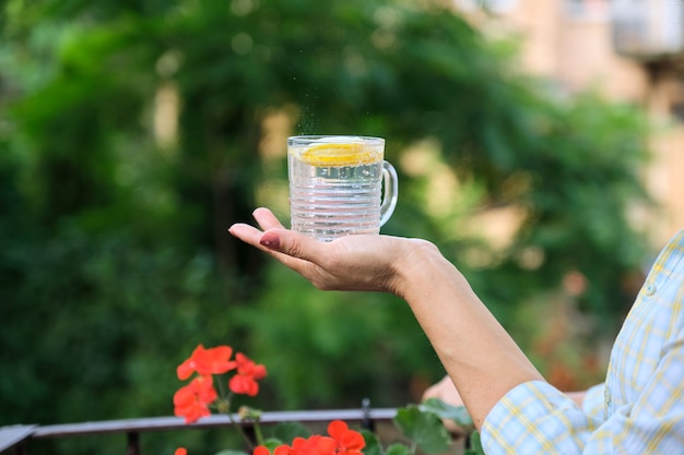 Nahaufnahme von Mineralwasser mit Zitronenscheibe in den Händen der Frau.