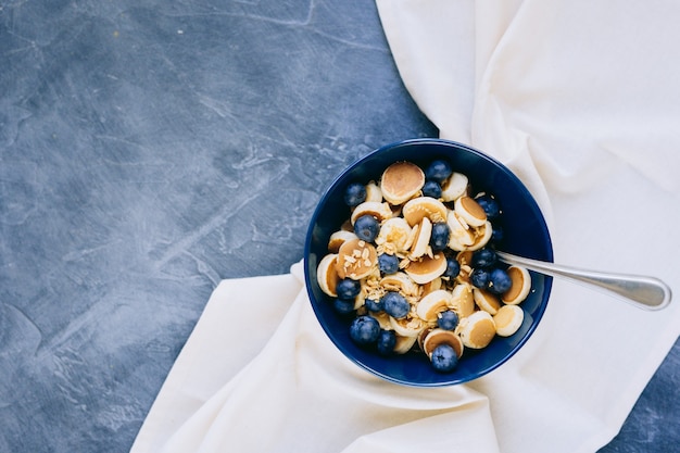 Foto nahaufnahme von mini-pfannkuchen-müsli, mini-pfannkuchen in einer dunkelblauen schüssel mit ahornsirup-honig mit blaubeeren.