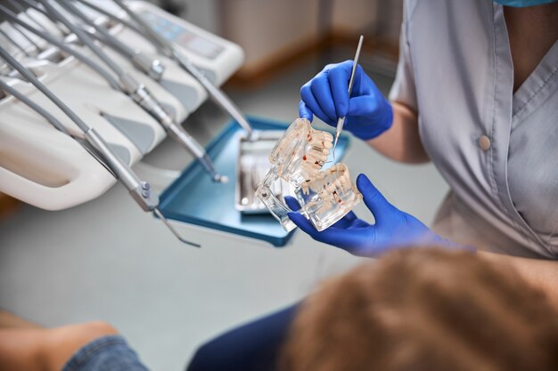 Nahaufnahme von Modellzähnen, die von einem Zahntechniker mit chirurgischen Handschuhen gehalten werden