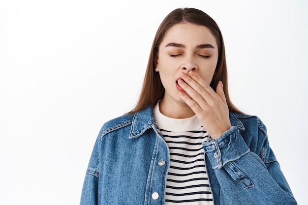 Nahaufnahme von müden Teenagern, die gähnen, Augen schließen und den Mund bedecken, während sie schläfrig gähnen, sich nach dem Lernen erschöpft fühlen und vor weißem Hintergrund stehen