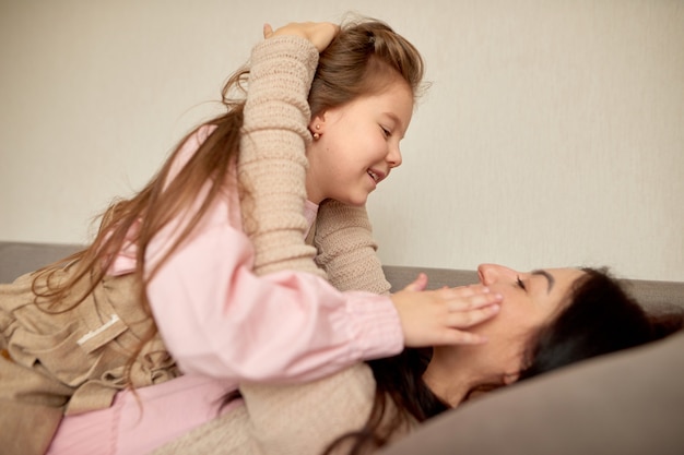 Nahaufnahme von niedlichen kleinen Vorschulmädchen spielen mit junger Mutter, kleine Tochter umarmen glückliche Mutter umarmen