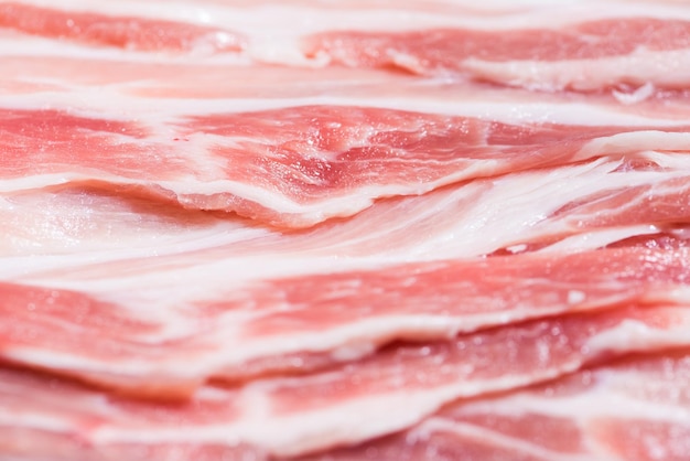 Nahaufnahme von oben Packung Speckstücke rohes Fleisch von frischem rotem Schweinefleisch mit weißen Fettscheiben werden in dünne Streifen geschnitten, die übereinander gestapelt sind