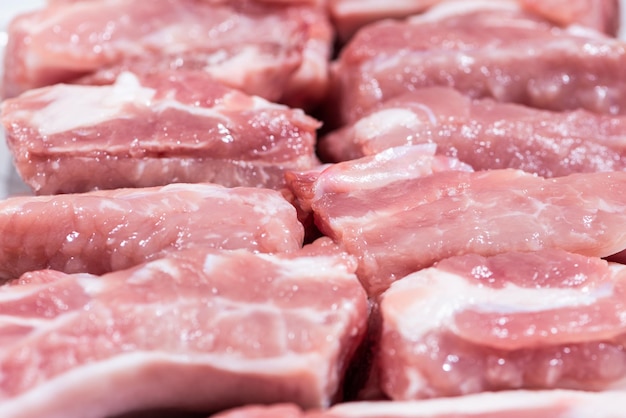 Nahaufnahme von oben Packungsstücke rohes Fleisch von Schweinelende auf Knochen frisches rotes Schweinefleisch mit weißem Fett der Schweinerippe In Stücke schneiden und in eine Reihe legen