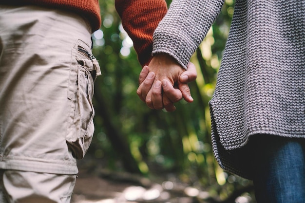 Nahaufnahme von Paarhändchenhalten mit grünem Waldnaturhintergrund. Konzept der Liebe und Beziehung zu erwachsenen Männern und Frauen heterosexuellen Menschen in Kontakt.