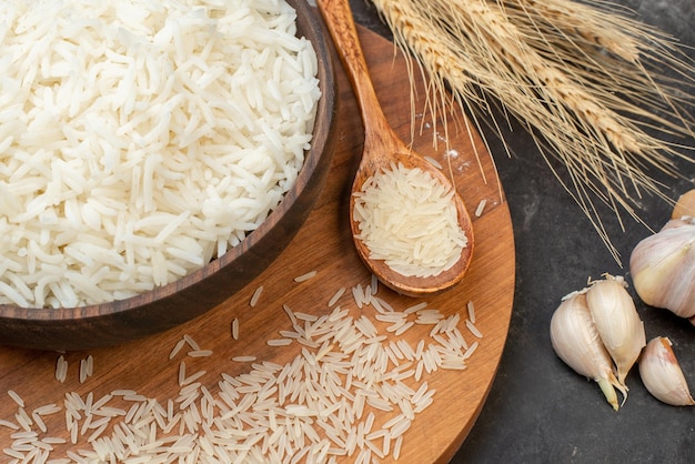 Nahaufnahme von perfektem Langreis in braunem Topf und auf Holzbrett-Knoblauch-Spike-Löffel auf grauem Hintergrund