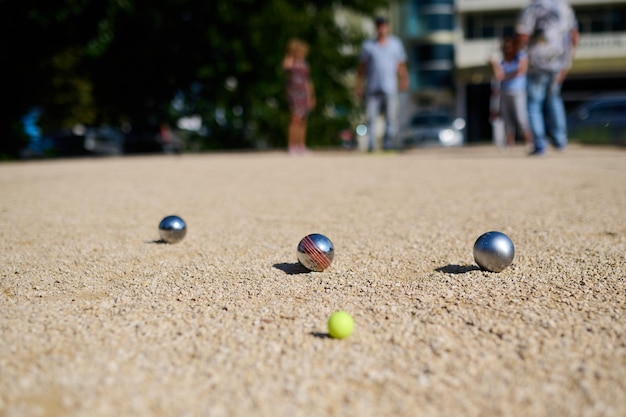 Nahaufnahme von Petanque-Bällen, die auf Kies verstreut sind, mit dem Zielball im Fokus, die glänzenden Metallkugeln