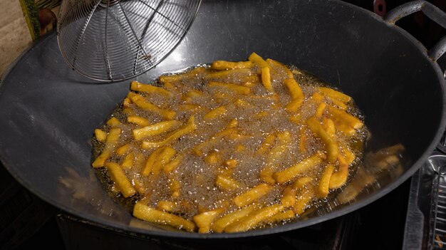 Nahaufnahme von Pommes Frites mit heißem Öl im dreckigen Wok am Marktstand für Straßenlebensmittel