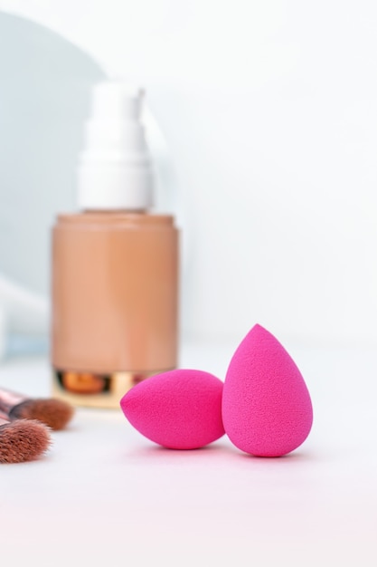 Nahaufnahme von rosa Schwamm und einer Flasche beige kosmetischer Grundierung, Pinsel für Make-up und Spiegel, Maskenbildner und Frauenzubehör