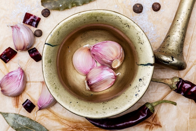 Nahaufnahme von rotem Knoblauch im Mörser mit anderen Gewürzen wie Chilischoten, schwarzem Pfeffer und Lorbeerblättern. Auf einem schönen rustikalen Vanillehintergrund. Draufsicht.