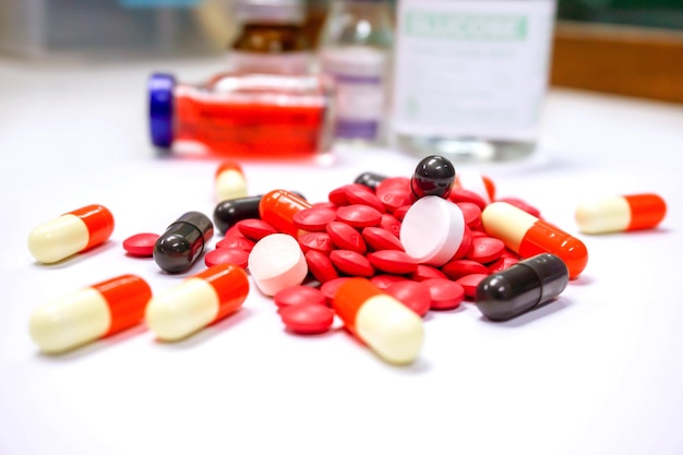 Nahaufnahme von roten Pillenmedikamenten und Kapselplatz auf weißem Tisch mit verschwommenem Hintergrund der Ampulle