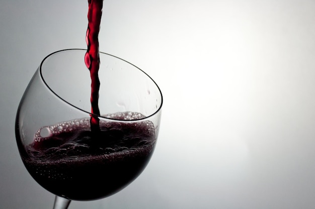 Nahaufnahme von Rotwein, das gegen weißen Hintergrund in ein Glas gegossen wird