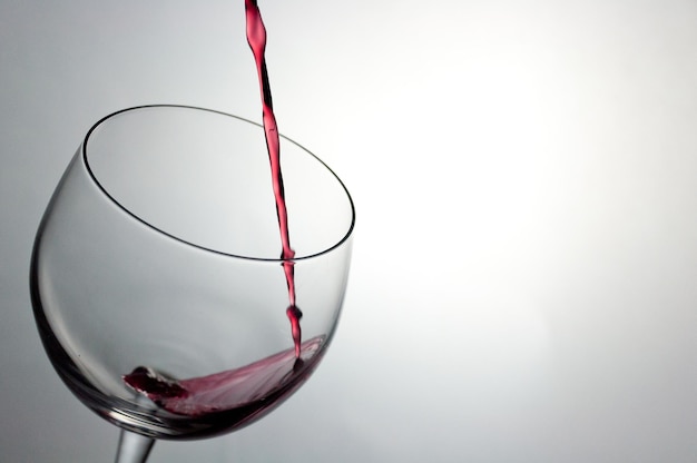Nahaufnahme von Rotwein, das gegen weißen Hintergrund in ein Glas gegossen wird
