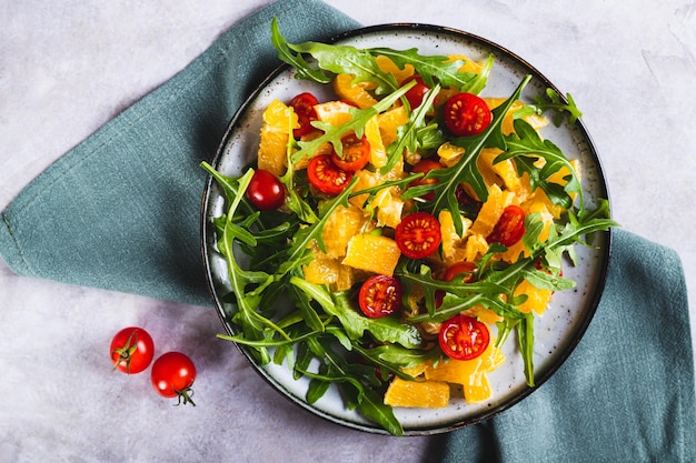 Nahaufnahme von Salat aus orangefarbenen Kirschtomaten und Arugula auf einem Teller auf der Tischplatte