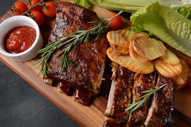 Nahaufnahme von Schweinerippchen gegrillt mit BBQ-Sauce und in Honig karamellisiert. Leckerer Snack zum Bier auf einem Holzbrett. Gegrillte Schweinerippchen mit Gewürzen auf Steinhintergrund