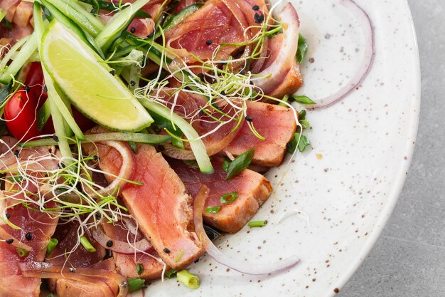 Nahaufnahme von seltenen gebratenen Thunfischscheiben mit Limetten- und Rucola-Blättern auf einem Teller.