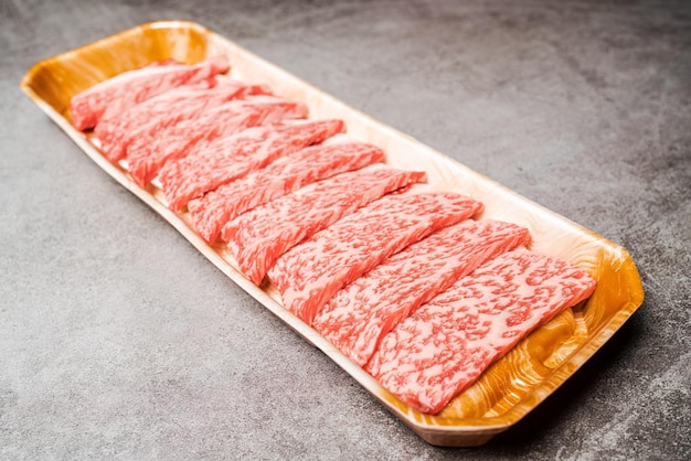 Nahaufnahme von seltenen Premium-Scheiben Sirloin Wagyu A5-Rindfleisch mit hochmarmorierter Textur auf einem Tablett, das für Yakiniku Sukiyaki und Shabu Place auf dem Hintergrund mit Kopierraum serviert wird