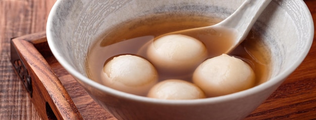 Nahaufnahme von Sesam Big Tangyuan (Tang Yuan, klebrige Reisknödelbällchen) mit süßer Sirupsuppe in einer Schüssel auf Holztischhintergrund für Wintersonnenwende-Festivalessen.