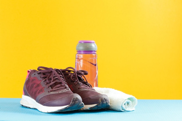 Nahaufnahme von Sportschuhen mit Wasserflasche und Serviette auf gelbem Hintergrund