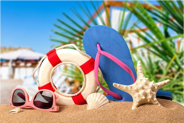 Nahaufnahme von Strandzubehör auf Sand. Flip-Flops, Sonnenbrille, Seesterne, Handtuch