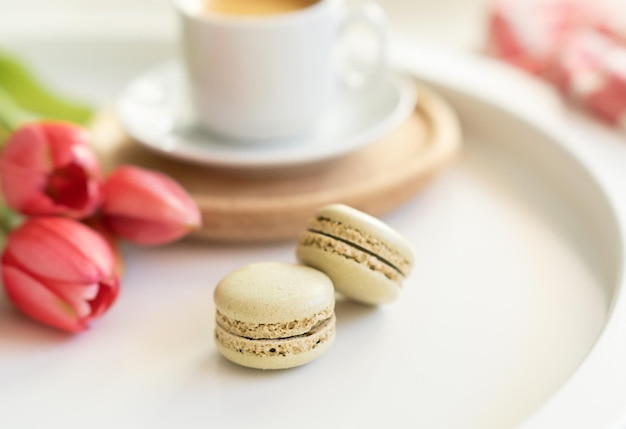 Nahaufnahme von süßen französischen Macarons Tasse Tee oder Kaffee und Frühlingsblumen auf weißem Hintergrund Platz für Text