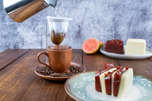 Nahaufnahme von süßen Guavenscheiben und Quark Im Hintergrund ein Mann, der heißes Wasser in einen Kaffeefilter aus Stoff gießt