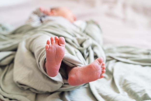 Nahaufnahme von süßen, winzigen, neugeborenen Füßen in einer weichen, grünen Decke