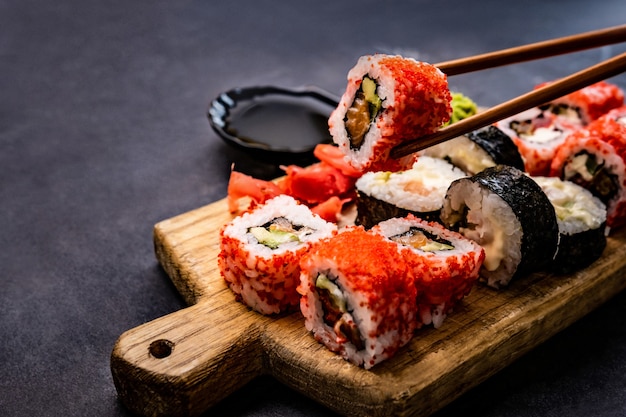 Nahaufnahme von Sushi Maki-Set serviert auf Holztablett Person Hand hält Rolle mit Essstäbchen japan...