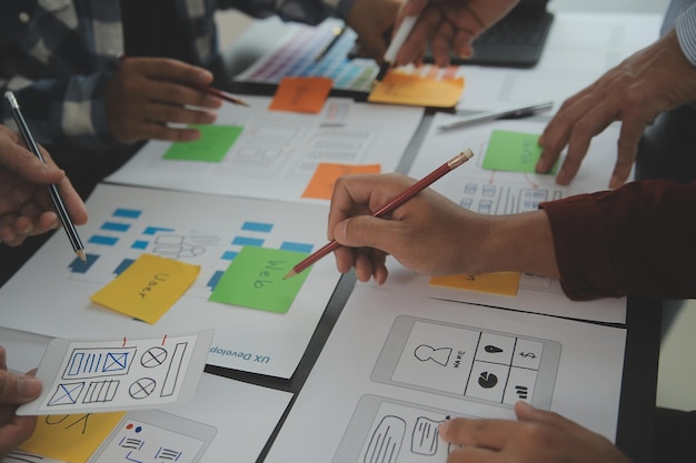 Nahaufnahme von ux-Entwicklern und ui-Designern beim Brainstorming über das Wireframe-Design der mobilen App-Schnittstelle auf dem Tisch mit Kundeninformationen und Farbcode in einer modernen Agentur für digitale Entwicklung im Büro