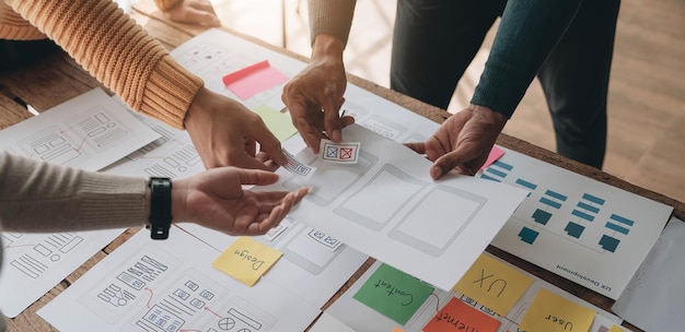 Nahaufnahme von ux-Entwicklern und ui-Designern beim Brainstorming über das Wireframe-Design der mobilen App-Schnittstelle auf dem Tisch mit Kundeninformationen und Farbcode in einer modernen Agentur für digitale Entwicklung im Büro