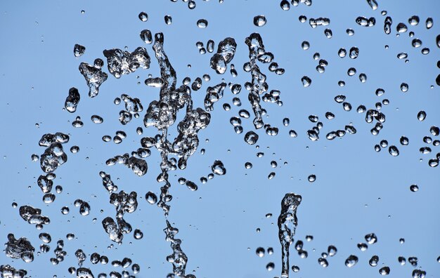 Nahaufnahme von Wassertropfen des Brunnenstroms über dem Hintergrund des klaren blauen Himmels spritzen