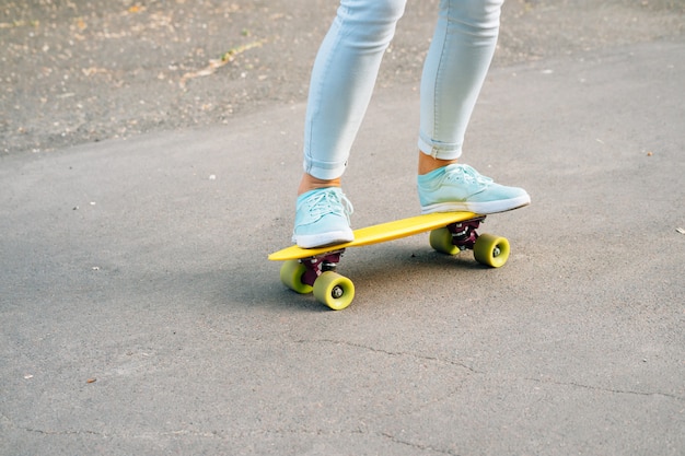 Nahaufnahme von weiblichen Beinen in den Jeans und in Turnschuhen, die ein Skateboard auf die Straße reiten